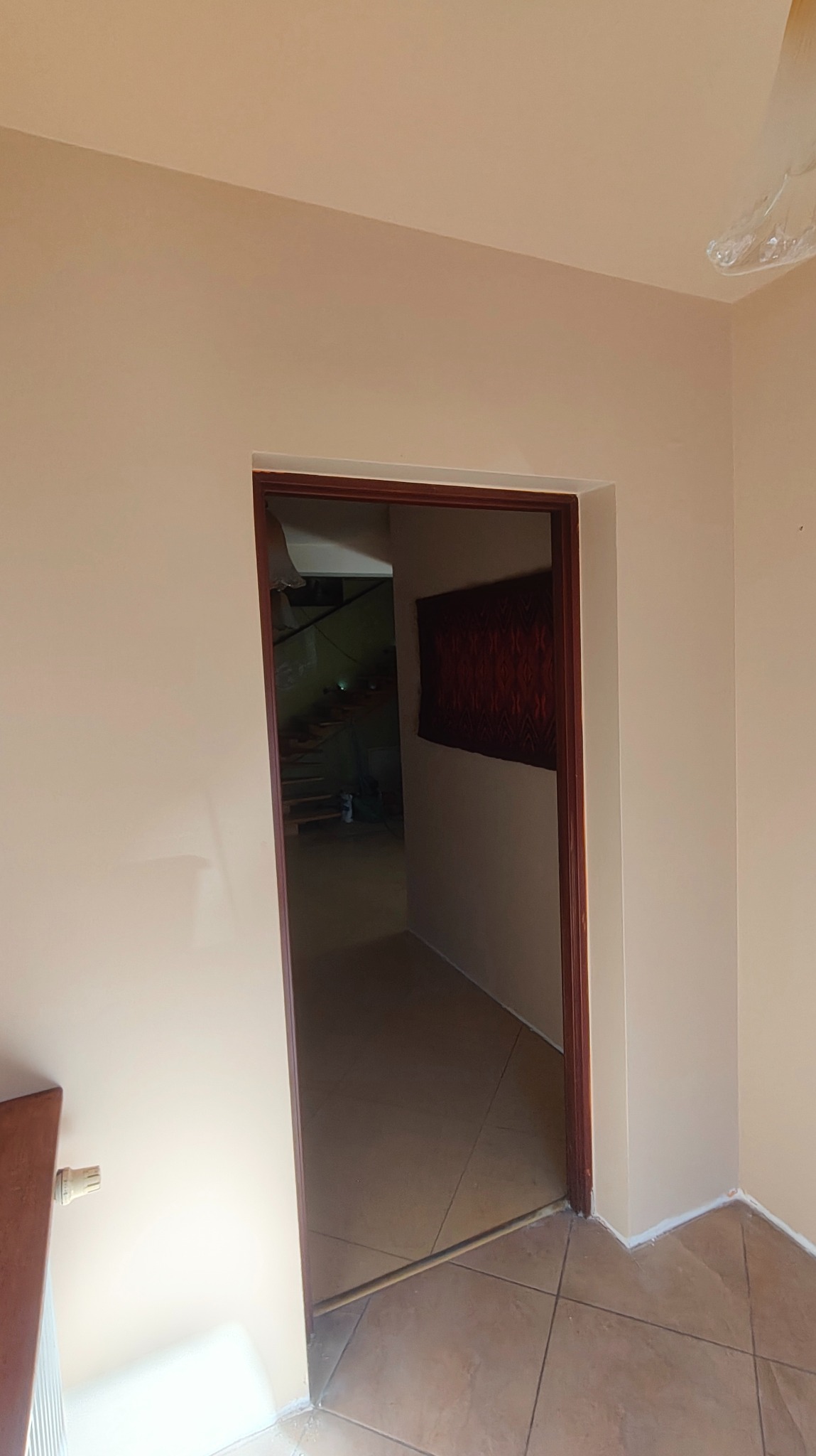 Jasne, świeżo pomalowane ściany w odcieniach beżu, widoczne przez otwarte drzwi z brązową ramą. W tle schody i dekoracja ścienna.