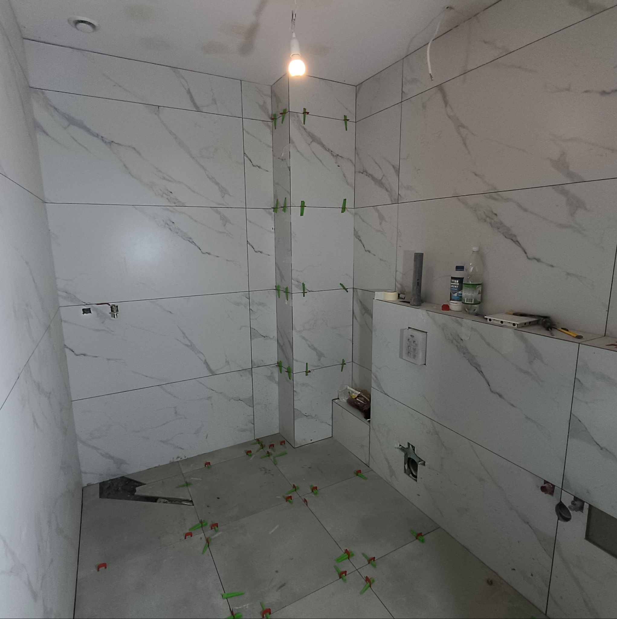 Łazienka w trakcie układania płytek imitujących marmur, widoczne krzyżyki dystansowe i narzędzia, surowy stan.