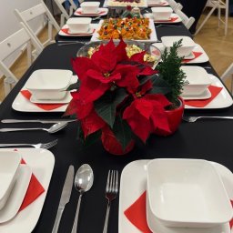 Praski Catering - Uroczysty stół z czarnym obrusem, nakryty białą zastawą, czerwonymi serwetkami i świątecznymi dekoracjami, gotowy na przyjęcie gości. Centralnie ustawiona czerwona gwiazda betlejemska.