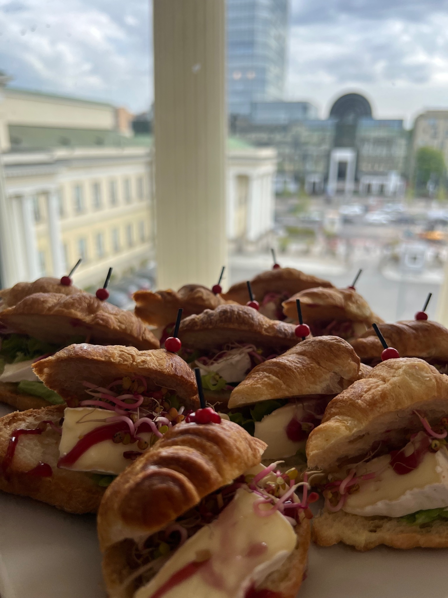 Kruche rogaliki z serem brie, awokado i kiełkami, podane na przyjęciu z widokiem na miasto w tle. Elegancki catering na event.