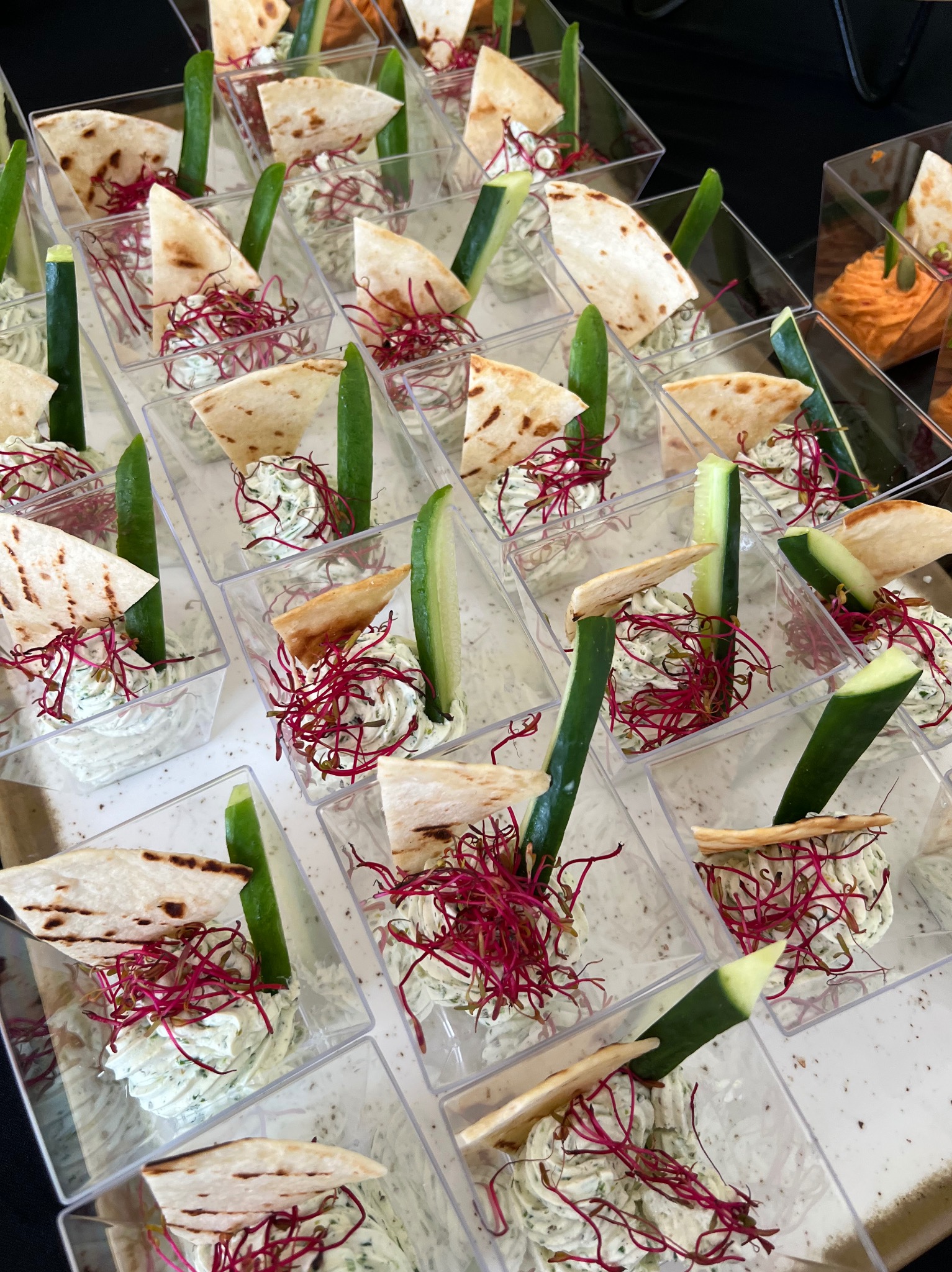 Eleganckie przekąski w przezroczystych pojemnikach: kremowy dip, pita, ogórek i czerwone kiełki. Idealne na firmowe przyjęcie lub świąteczny catering.