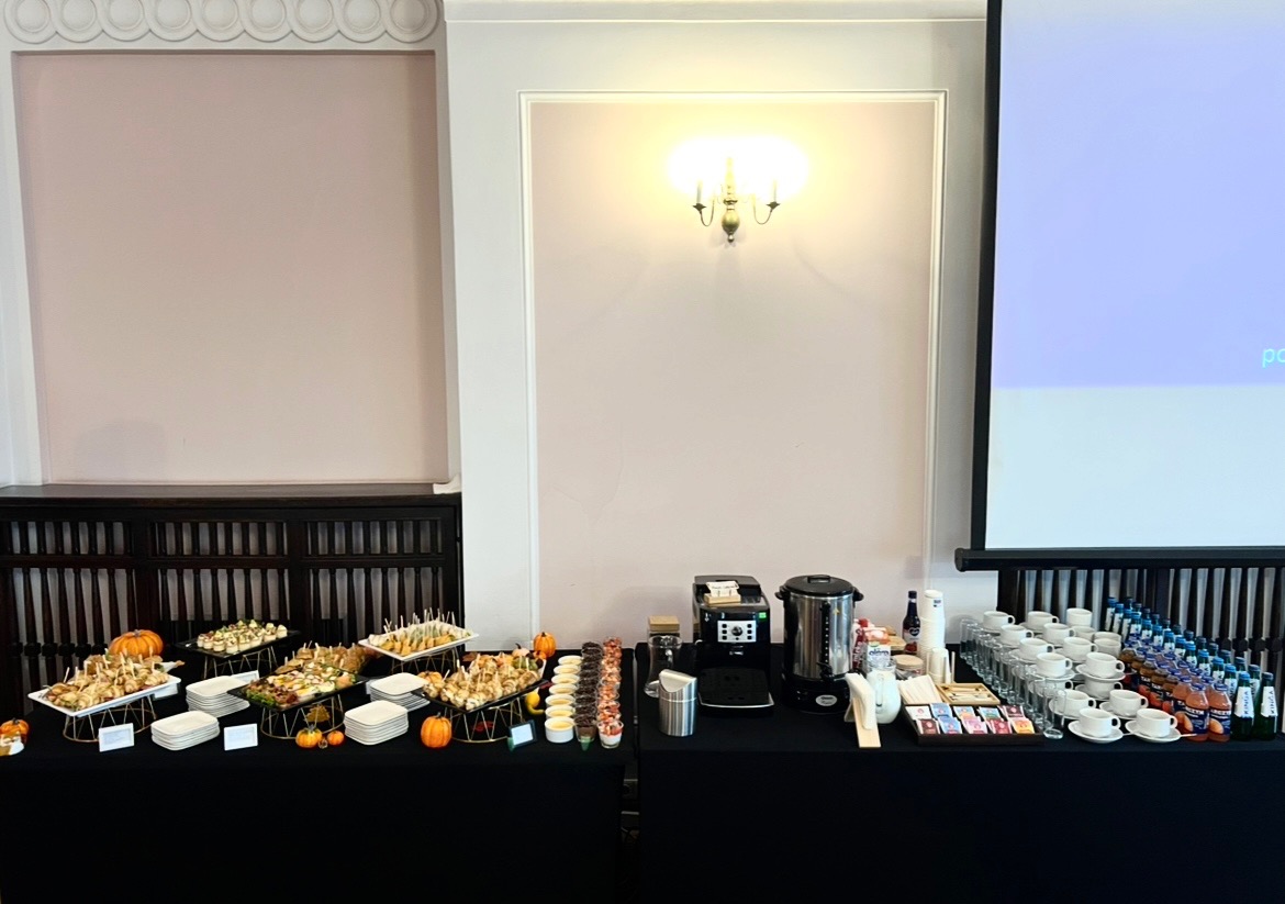 Stół cateringowy z przekąskami, napojami i dekoracjami dyniowymi, przygotowany na eleganckie wydarzenie w jasnym wnętrzu z projektorem.