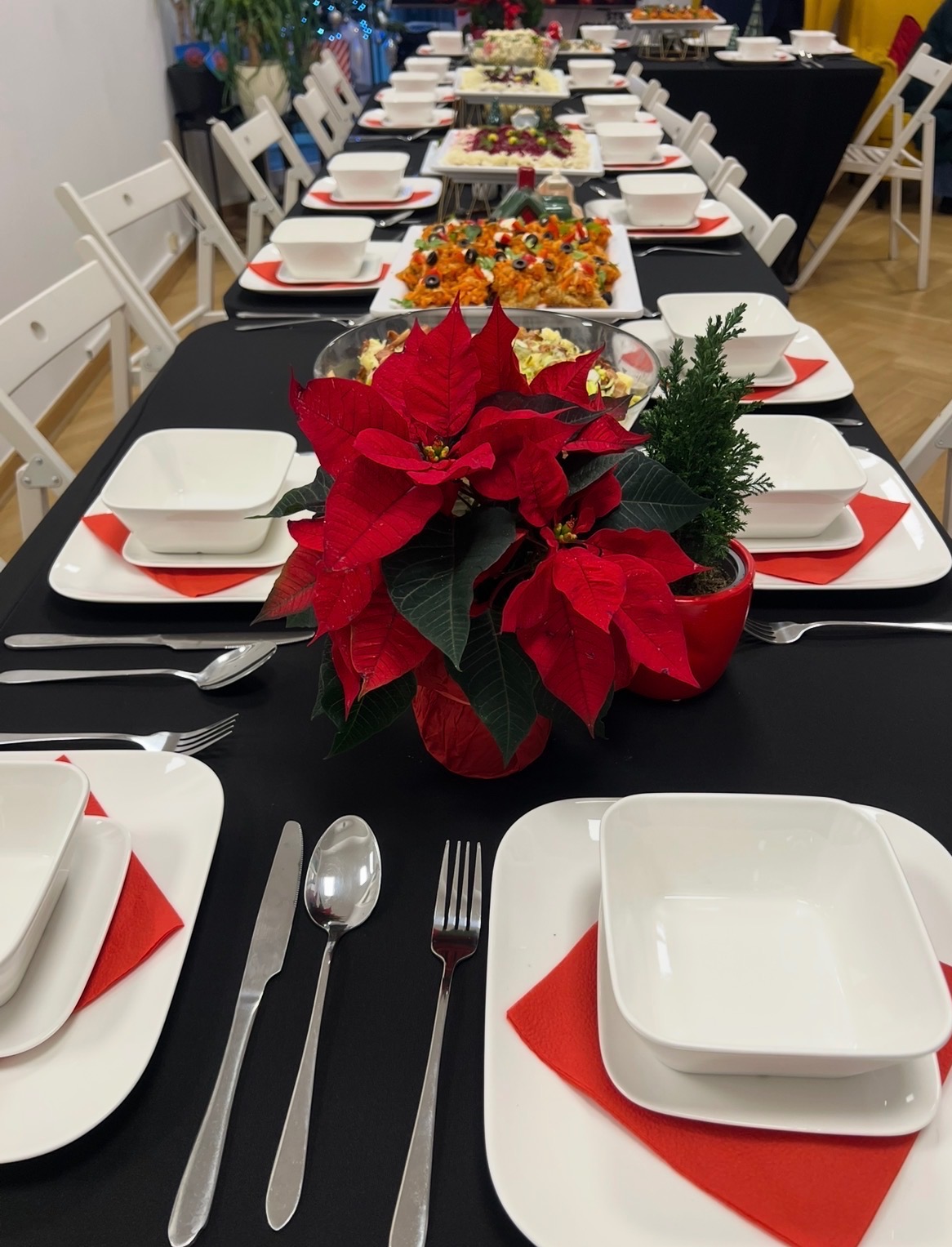 Uroczysty stół z czarnym obrusem, nakryty białą zastawą, czerwonymi serwetkami i świątecznymi dekoracjami, gotowy na przyjęcie gości. Centralnie ustawiona czerwona gwiazda betlejemska.
