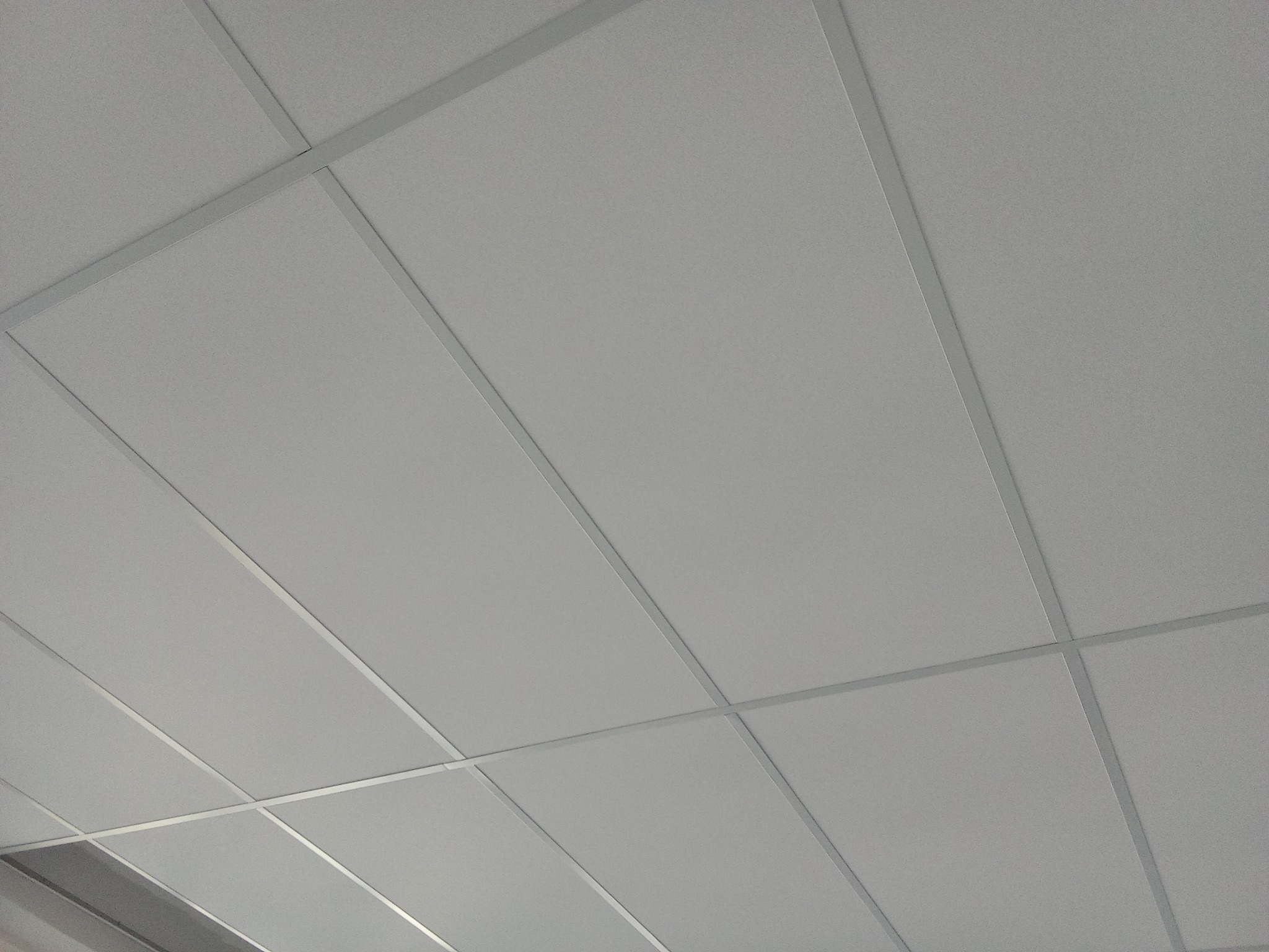 Kwadratowa, biała kaseta sufitowa z widoczną metalową konstrukcją nośną, sfotografowana pod kątem.