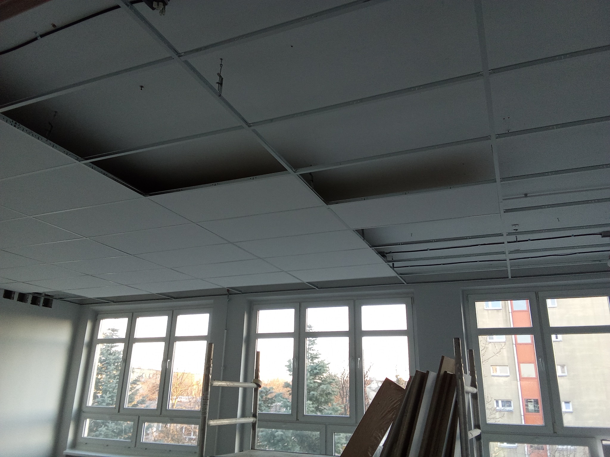 Montaż sufitu podwieszanego kasetonowego w pomieszczeniu biurowym; widoczne okna i drabina oparta o ścianę.