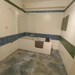Wykończona łazienka w Biłgoraju z wanną z bocznym wejściem, wyłożona płytkami w odcieniach bieli, niebieskiego i zieleni. Na podłodze płytki imitujące kamień.