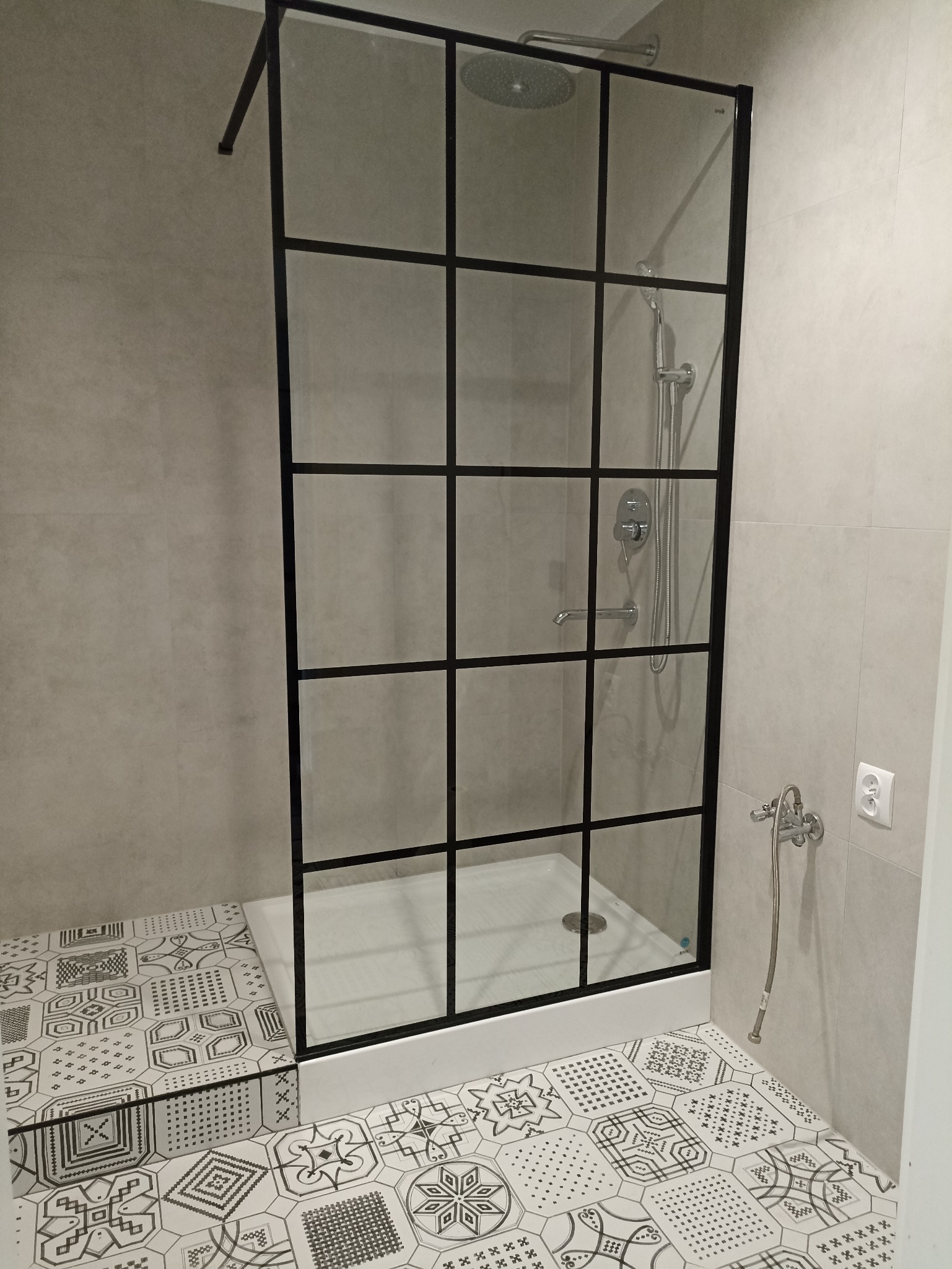 Nowoczesna kabina prysznicowa z czarną ramą i wzorzystymi płytkami podłogowymi. Minimalistyczny design, szklane ścianki, chromowana armatura i jasne, neutralne kolory.