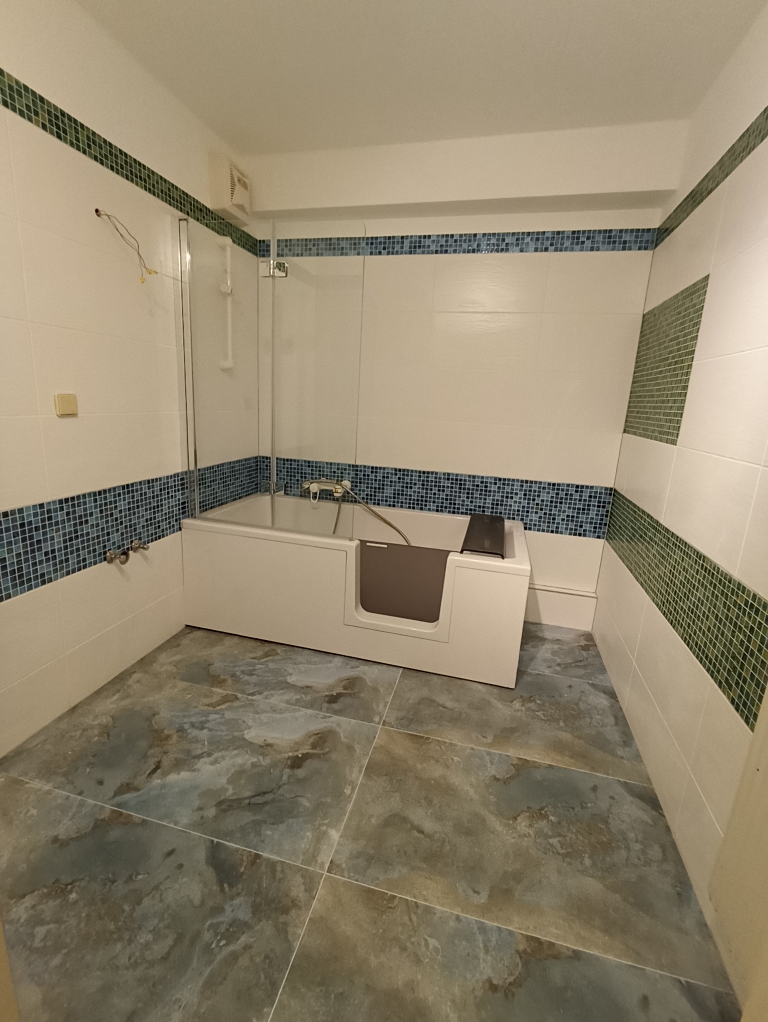 Wykończona łazienka w Biłgoraju z wanną z bocznym wejściem, wyłożona płytkami w odcieniach bieli, niebieskiego i zieleni. Na podłodze płytki imitujące kamień.