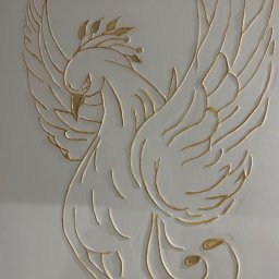 GK - Dekoracyjna płaskorzeźba przedstawiająca feniksa z gałązką oliwną na białej ścianie, wykonana ze złotej masy szpachlowej.