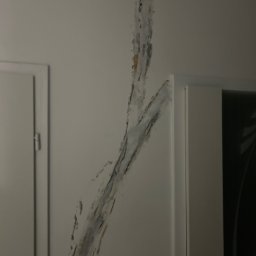 GK - Ślady po zalaniu na ścianie, widoczne zacieki i uszkodzenia powłoki malarskiej, obok framuga drzwi.