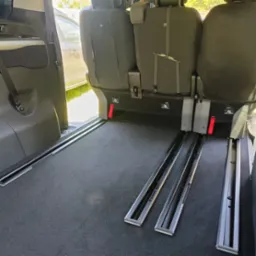 Wnętrze busa z systemem szynowym do mocowania foteli. Widoczne szyny w podłodze i mocowania ISOFIX. Otwarte drzwi boczne pojazdu.