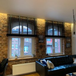 Igor Kravets - Czarne żaluzje drewniane w oknach o łukowym kształcie, na tle ceglanej ściany w salonie. Widok na budynek z zewnątrz. Ciepłe oświetlenie podkreśla fakturę cegły.