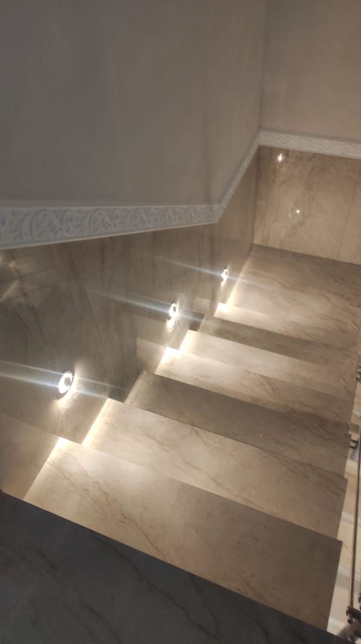 Schody wyłożone marmurkową płytką z podświetleniem LED w ścianie, widok z góry, dekoracyjny gzyms sufitowy.