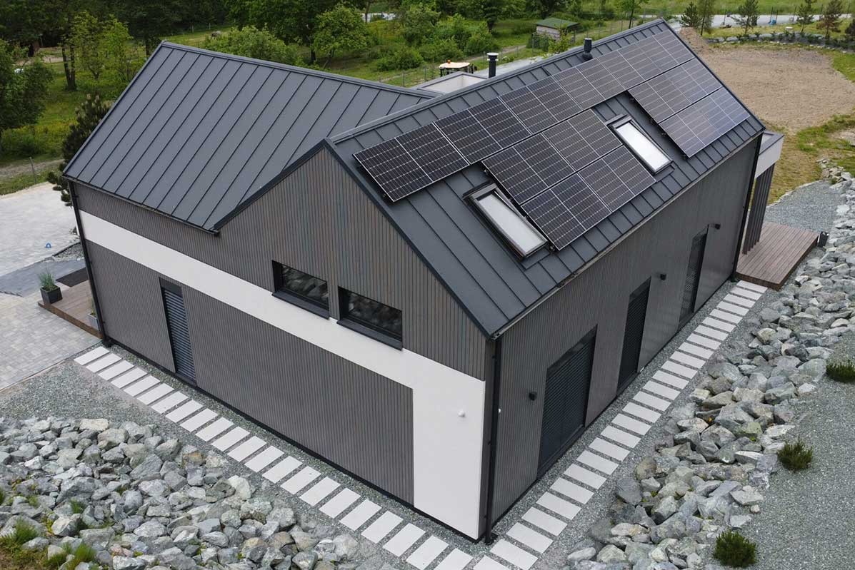 Nowoczesny dom z szarej blachy z panelami słonecznymi na dachu, otoczony kamiennym ogrodem i ścieżką z płyt.