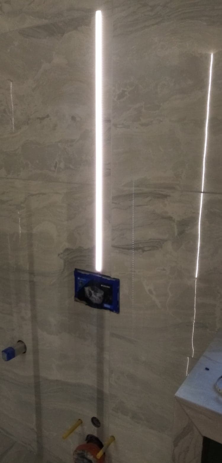 Ściana w łazience wykończona marmurowymi płytkami z wbudowanym oświetleniem LED. Widoczne elementy instalacji wodnej i podtynkowej.