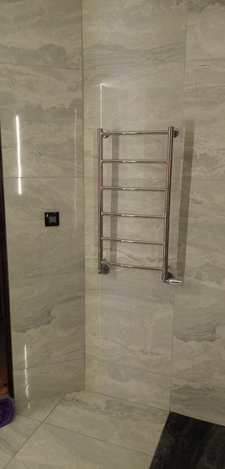 Wykończona łazienka: płytki imitujące marmur, grzejnik drabinkowy, czarny przełącznik światła. Nowoczesny design i dbałość o detale.