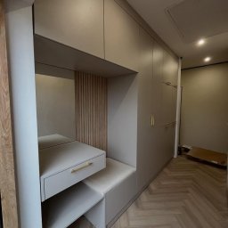 LAJTNER INTERIORS SPÓŁKA Z OGRANICZONĄ ODPOWIEDZIALNOŚCIĄ - Szara szafa wnękowa z siedziskiem i toaletką z lustrem, drewniane lamele dekoracyjne na ścianie, parkiet w jodełkę.