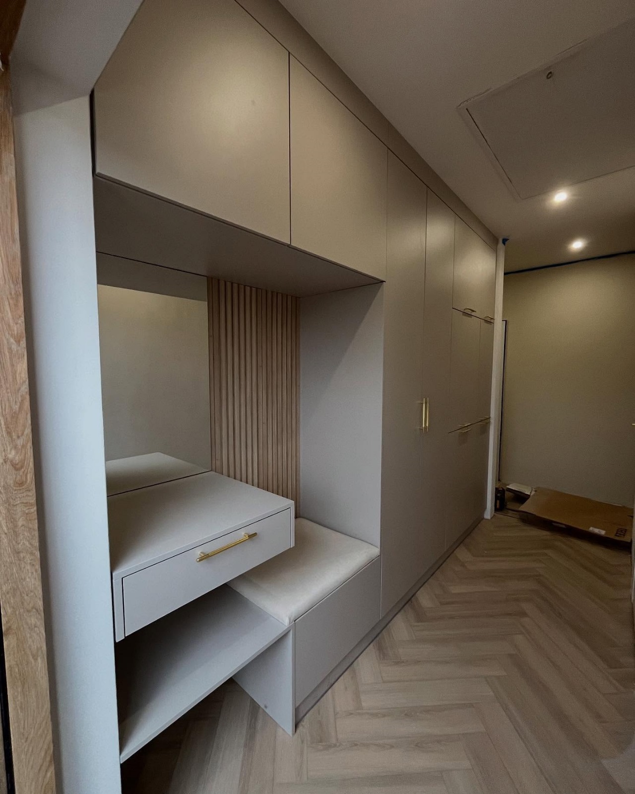 Szara szafa wnękowa z siedziskiem i toaletką z lustrem, drewniane lamele dekoracyjne na ścianie, parkiet w jodełkę.