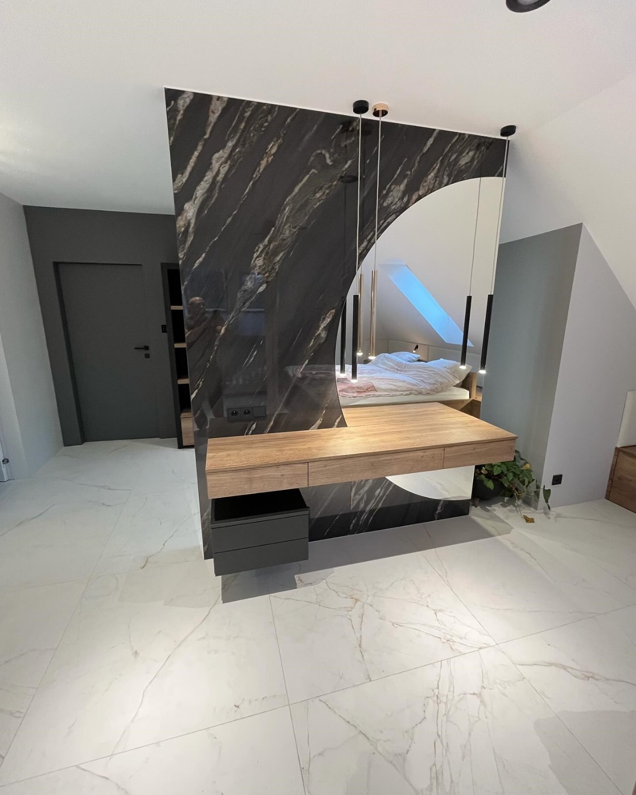 Nowoczesna toaletka z drewnianym blatem i czarną marmurową okładziną, wbudowana w ścianę, z widocznym odbiciem sypialni w lustrze, oświetlenie punktowe.