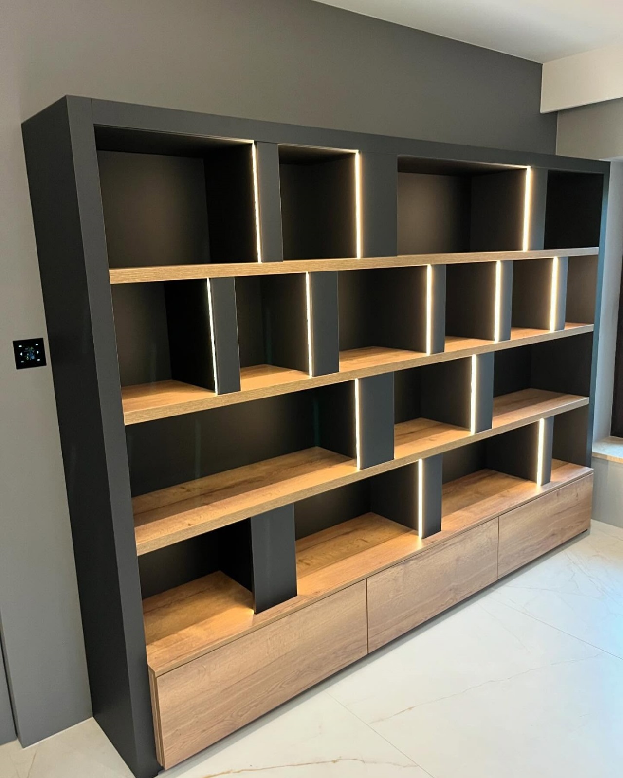 Nowoczesna szafa wnękowa z szarymi elementami i drewnianymi półkami, podświetlana pionowymi paskami LED, z dolnymi szufladami w kolorze drewna.