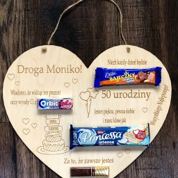 A&K Studio - Drewniane serce z wygrawerowanymi życzeniami urodzinowymi i przymocowanymi słodyczami, leżące na drewnianym tle.