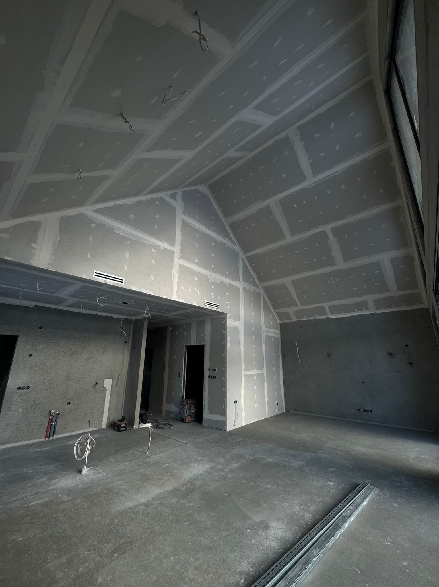 Wnętrze w trakcie wykańczania: sufit i ściany pokryte płytami kartonowo-gipsowymi, widoczne łączenia i szpachlowanie. Na podłodze leżą profile. Surowy stan.
