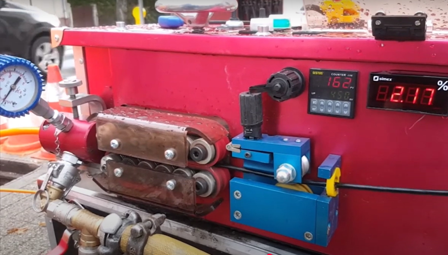 Urządzenie do obróbki kabli telekomunikacyjnych z wyświetlaczami, manometrem i elementami hydraulicznymi, widoczne elementy sterujące i przewód w trakcie obróbki.