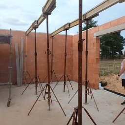 Len-Bud - Wnętrze wznoszonego domu z czerwonej cegły ceramicznej, widoczne stemple budowlane podtrzymujące nadproża, rusztowanie i mężczyzna w tle.