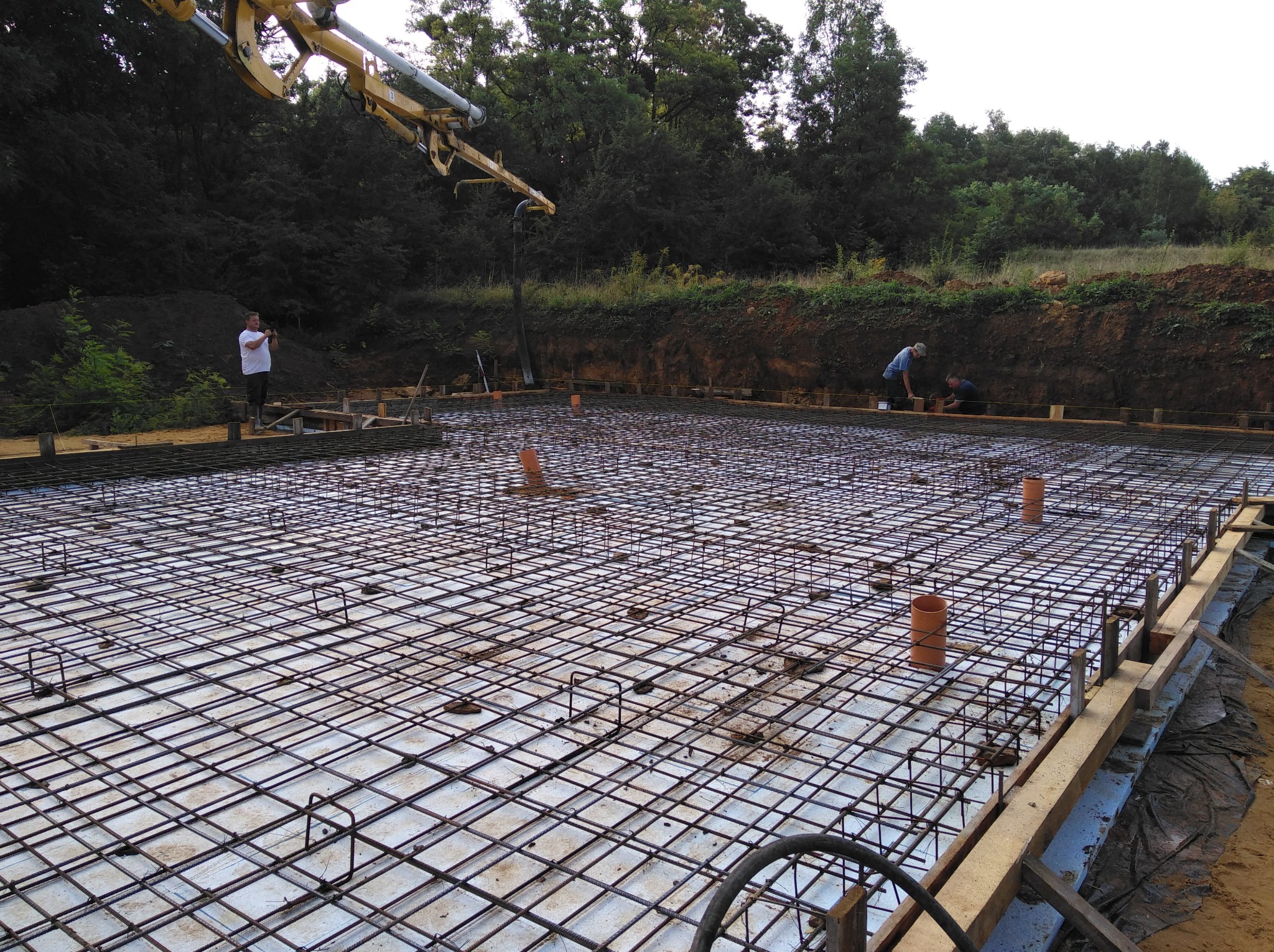 Zbrojenie fundamentu z wylewką betonu z pompy, widoczni pracownicy i drewniane szalunki.