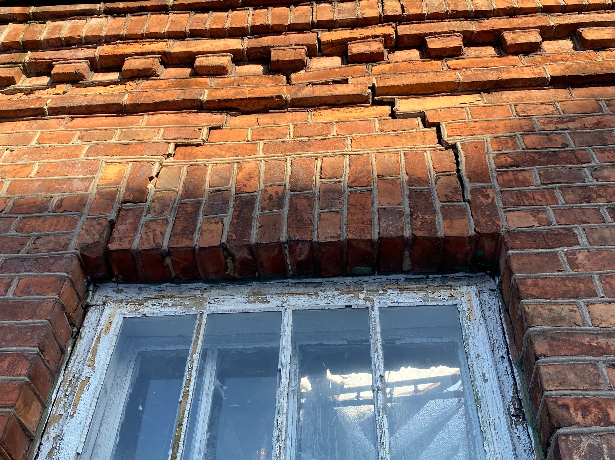 Pęknięcie w murze z czerwonej cegły nad oknem z łuszczącą się, białą farbą.