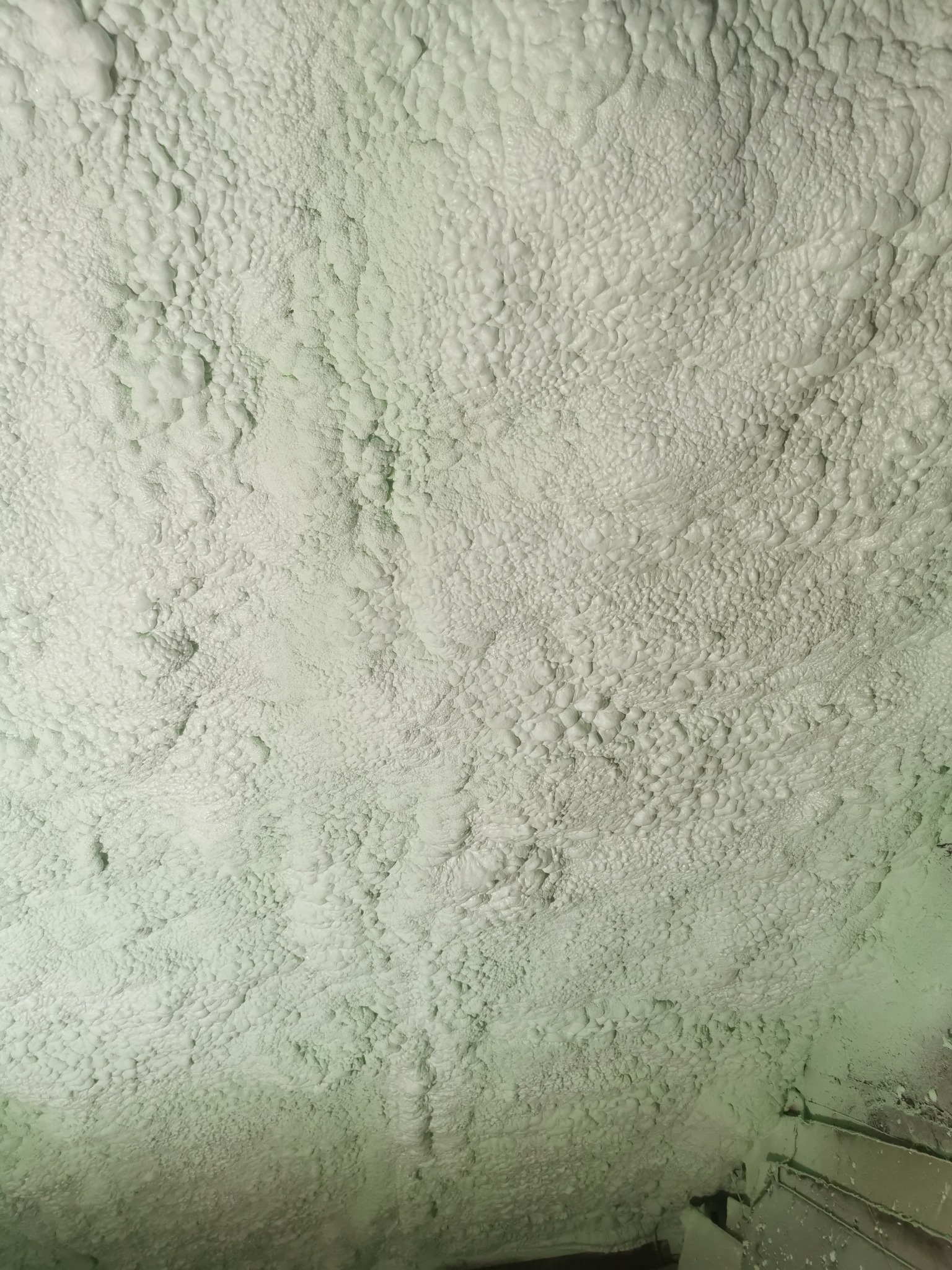 Szczegółowe ujęcie warstwy jasnej pianki PUR o nieregularnej strukturze, pokrywającej powierzchnię. Widoczne nierówności i porowatość materiału izolacyjnego.