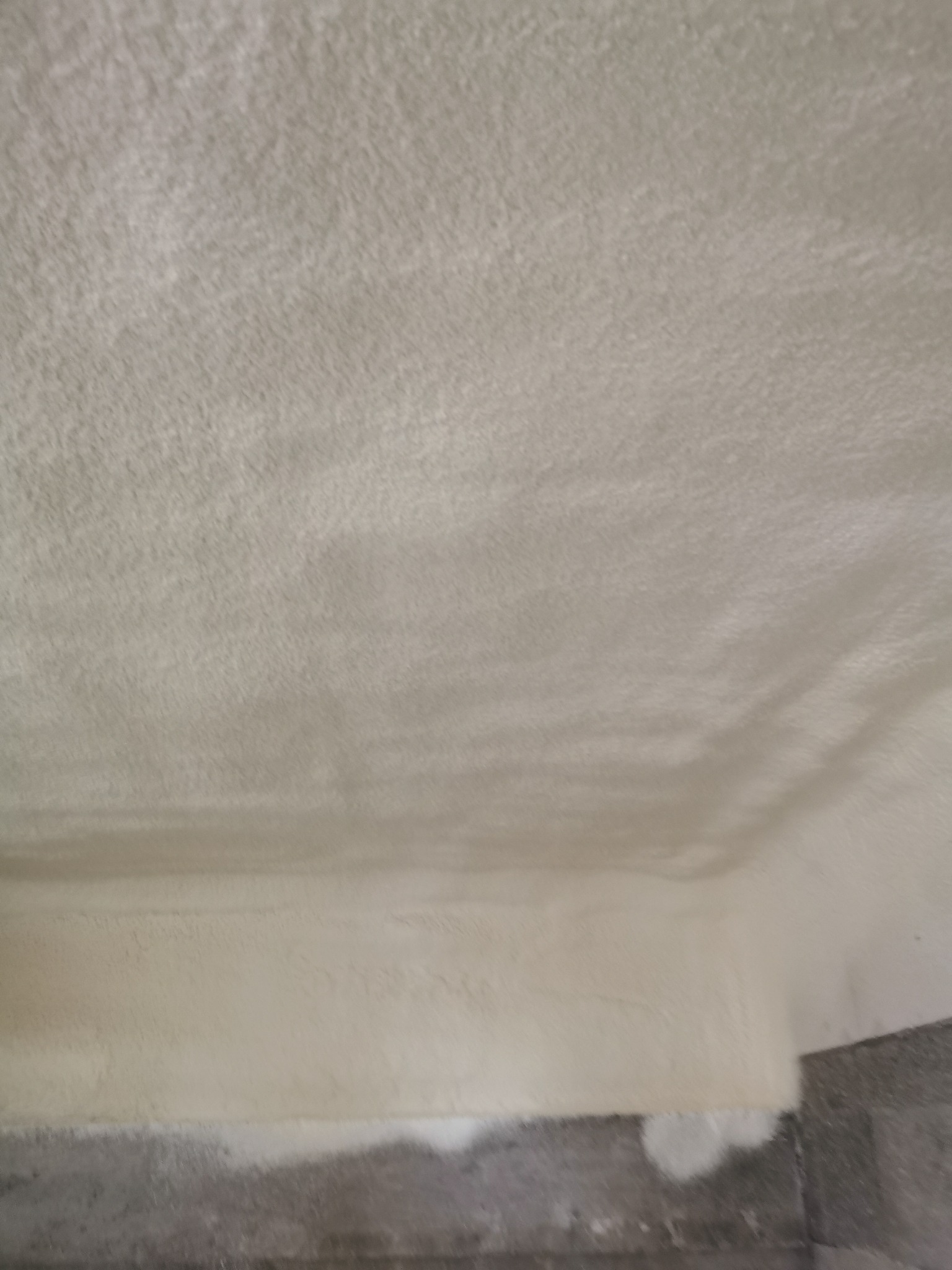 Poddasze po ociepleniu pianką PUR, widoczna struktura pianki na suficie i ścianie, blisko krawędzi podłogi. Szary beton w dolnej części kadru.