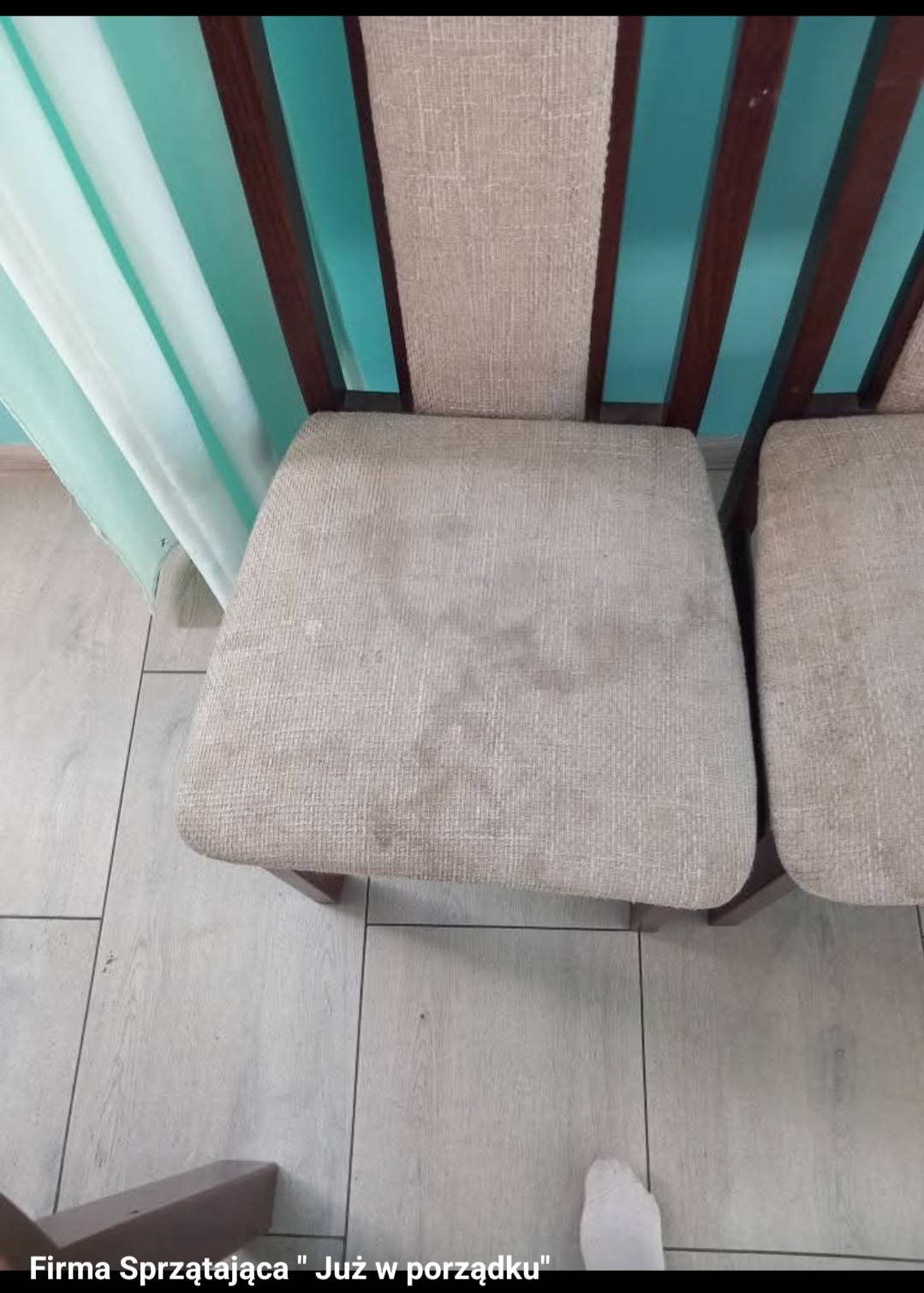 Brudne krzesło z tapicerowanym siedziskiem, widoczne plamy i zabrudzenia. Ujęcie z góry, fragment podłogi i zasłony w tle. Widoczny fragment stopy.