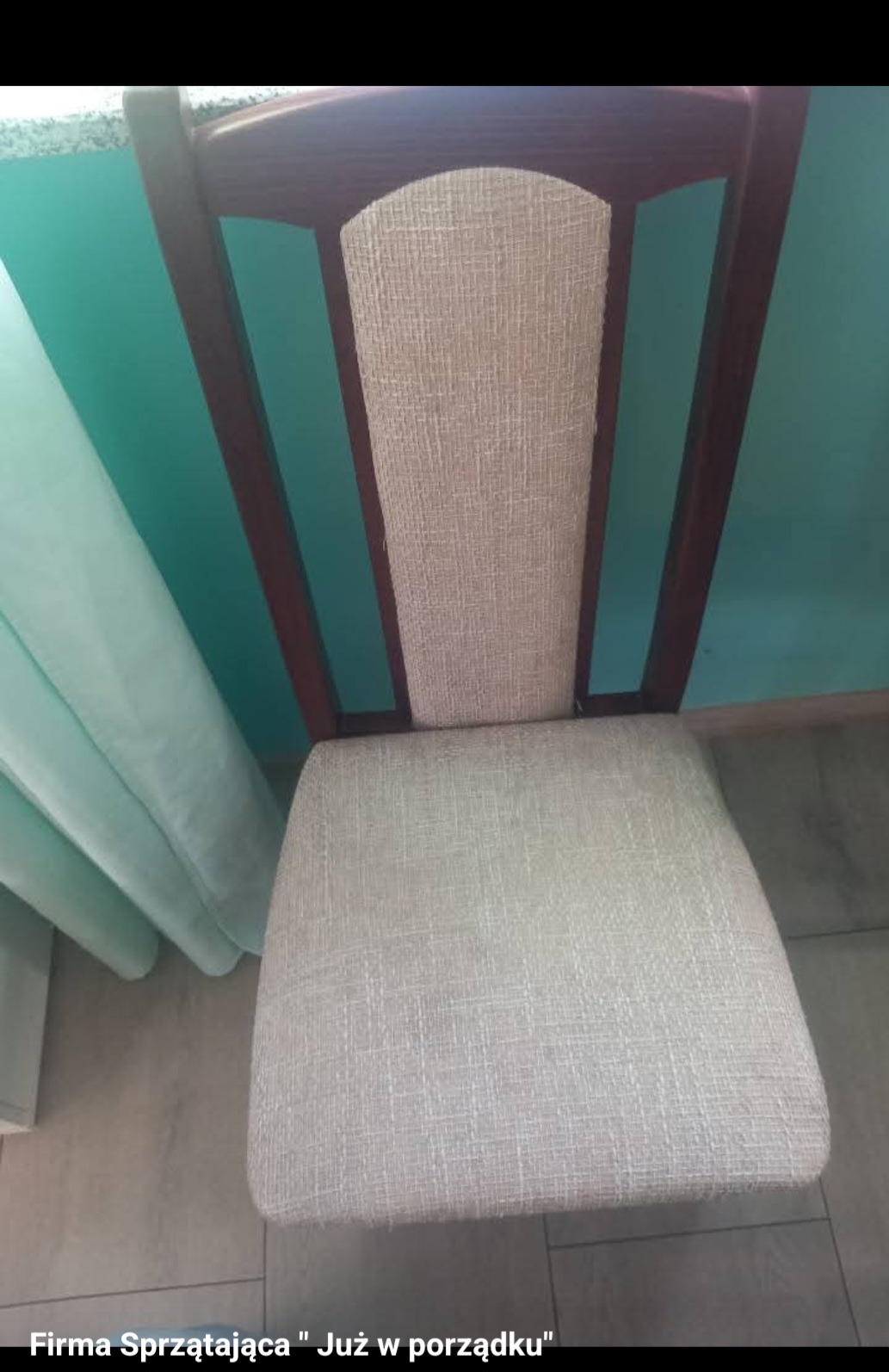 Krzesło z tapicerowanym siedziskiem i oparciem, brązowe drewniane nogi, na tle turkusowej ściany i zasłony. Widok z góry na czyste krzesło.