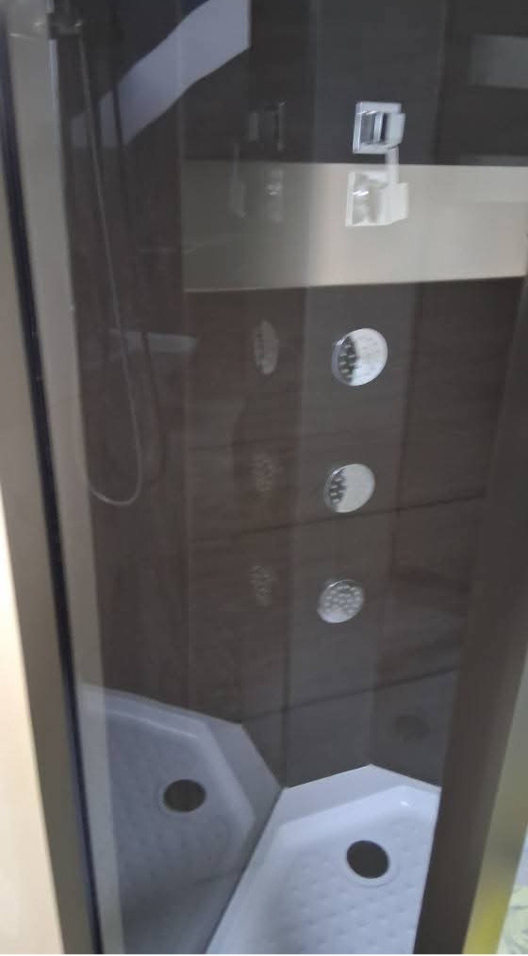 Kabina prysznicowa z hydromasażem i deszczownicą, widoczna przez szklane drzwi. Nowoczesny design, ciemne płytki, biały brodzik. Elementy chromowane.