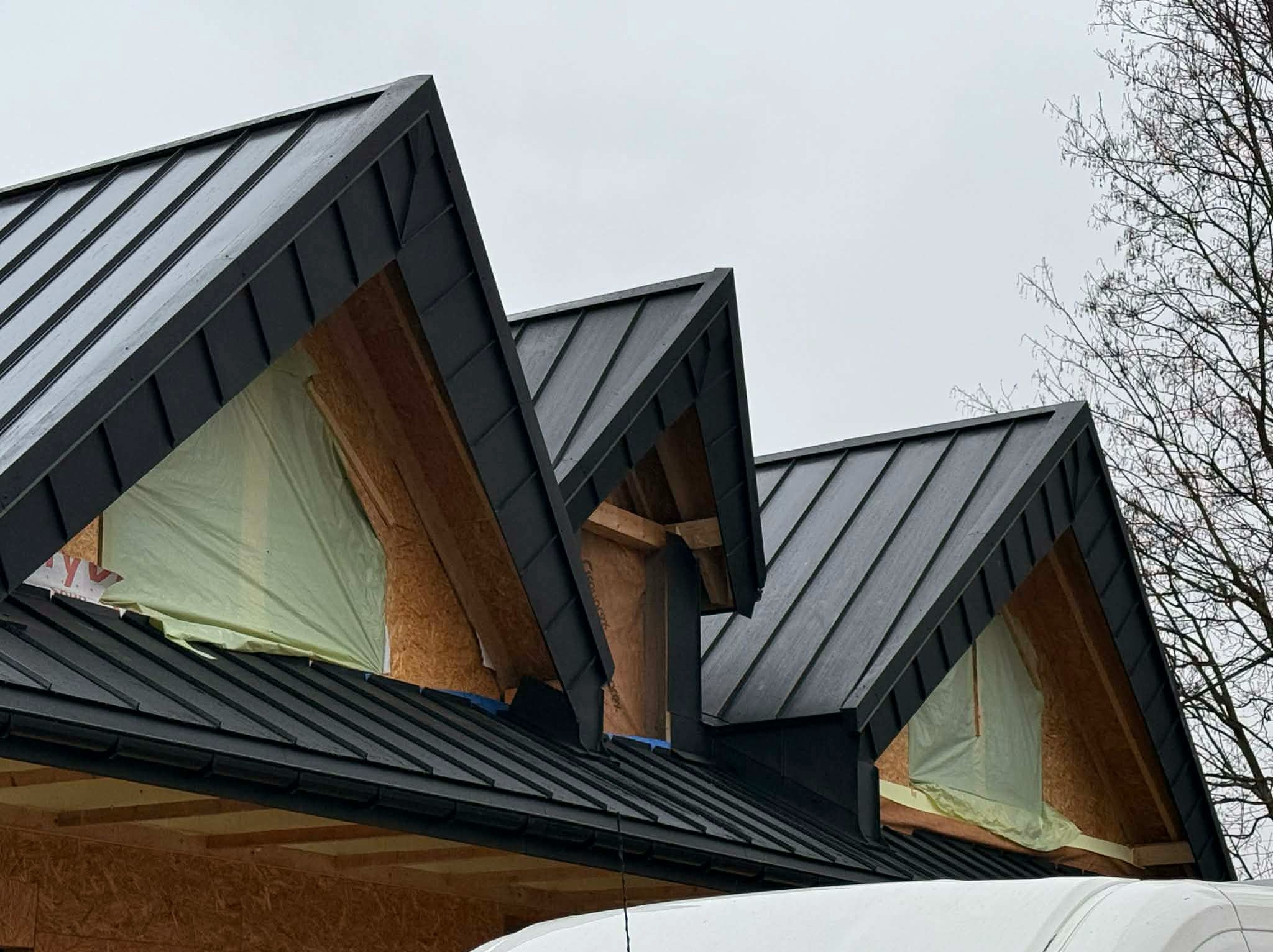 Nowoczesny, czarny dach z blachy na domu w trakcie budowy. Widoczne okna dachowe zabezpieczone folią. Minimalistyczny design i precyzyjne wykonanie.