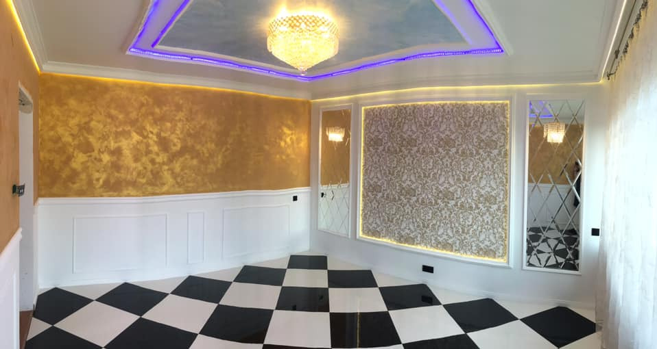 Eleganckie wnętrze po remoncie: złota ściana z dekoracyjną fakturą, biała boazeria, podłoga w czarno-białą szachownicę, sufit z niebieskim akcentem i kryształowym żyrandolem, oświetlenie LED...