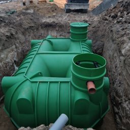 BIOLEN GRZEGORZ RYBIŃSKI - Zielony zbiornik z tworzywa sztucznego umieszczony w wykopie, widoczny fragment rury, w tle koparka Kubota i pryzma ziemi.