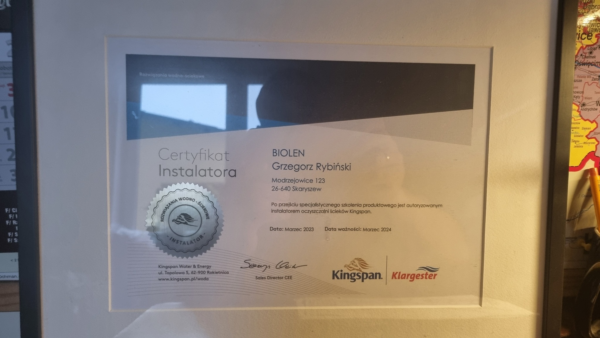 Oprawiony certyfikat instalatora systemów wodno-ściekowych Biolen Grzegorza Rybińskiego z datą ważności do marca 2024, z logo Kingspan Klargester, wiszący obok mapy Polski.