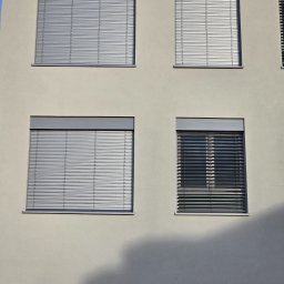 ZPHU BARTEK - Elewacja budynku z czterema oknami wyposażonymi w poziome osłony przeciwsłoneczne; trzy z nich są w pełni zasłonięte, jedno częściowo otwarte, rzucając cień na fasadę.