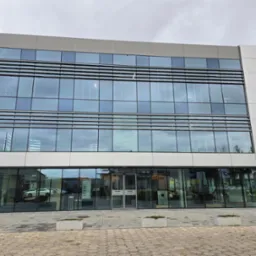 Nowoczesny budynek biurowy z szarymi poziomymi panelami przeciwsłonecznymi na fasadzie, widok z zewnątrz na ulicę Przemysłową 11.