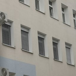 ZPHU BARTEK - Elewacja budynku z oknami osłoniętymi poziomymi listwami, z zamontowanymi klimatyzatorami na ścianie.