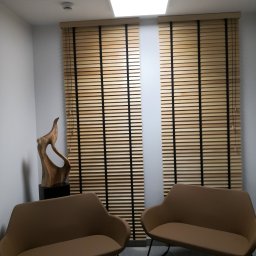 ZPHU BARTEK - Nowoczesne wnętrze z dwoma brązowymi sofami, drewnianą rzeźbą i oknami zasłoniętymi jasnymi lamelami z ciemnymi taśmami.