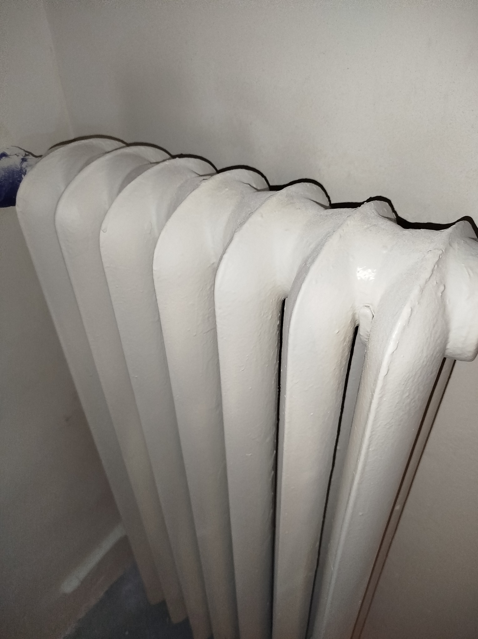 Żeliwny grzejnik pomalowany na biało, widoczne niedociągnięcia malarskie i zacieki farby.