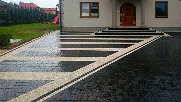 Ułożona nawierzchnia z kostki brukowej w geometryczny wzór przed domem, kontrastowe kolory, widoczne schody wejściowe.