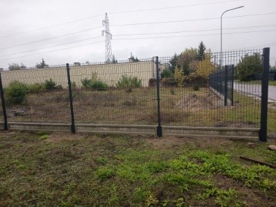 Nowoczesne ogrodzenie panelowe z podmurówką betonową, widok z zewnątrz na tle pochmurnego nieba i słupa wysokiego napięcia. Minimalistyczny design.