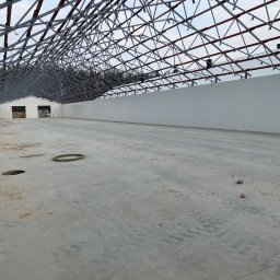 Twój Dach - Konstrukcja stalowa dachu hali przemysłowej w trakcie budowy, widok od wewnątrz. Stalowa więźba dachowa z elementami drewnianymi, ściany z płyt warstwowych.