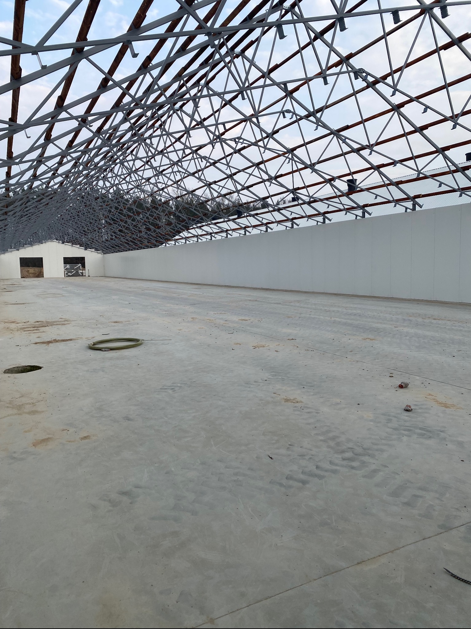 Konstrukcja stalowa dachu hali przemysłowej w trakcie budowy, widok od wewnątrz. Stalowa więźba dachowa z elementami drewnianymi, ściany z płyt warstwowych.