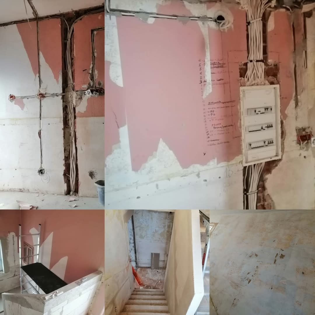 Wnętrze w trakcie remontu: odsłonięte przewody elektryczne, częściowo usunięta stara farba, widoczne ślady po gładzi, rozdzielnia elektryczna, schody w stanie surowym, rusztowanie w pomieszczeniu.