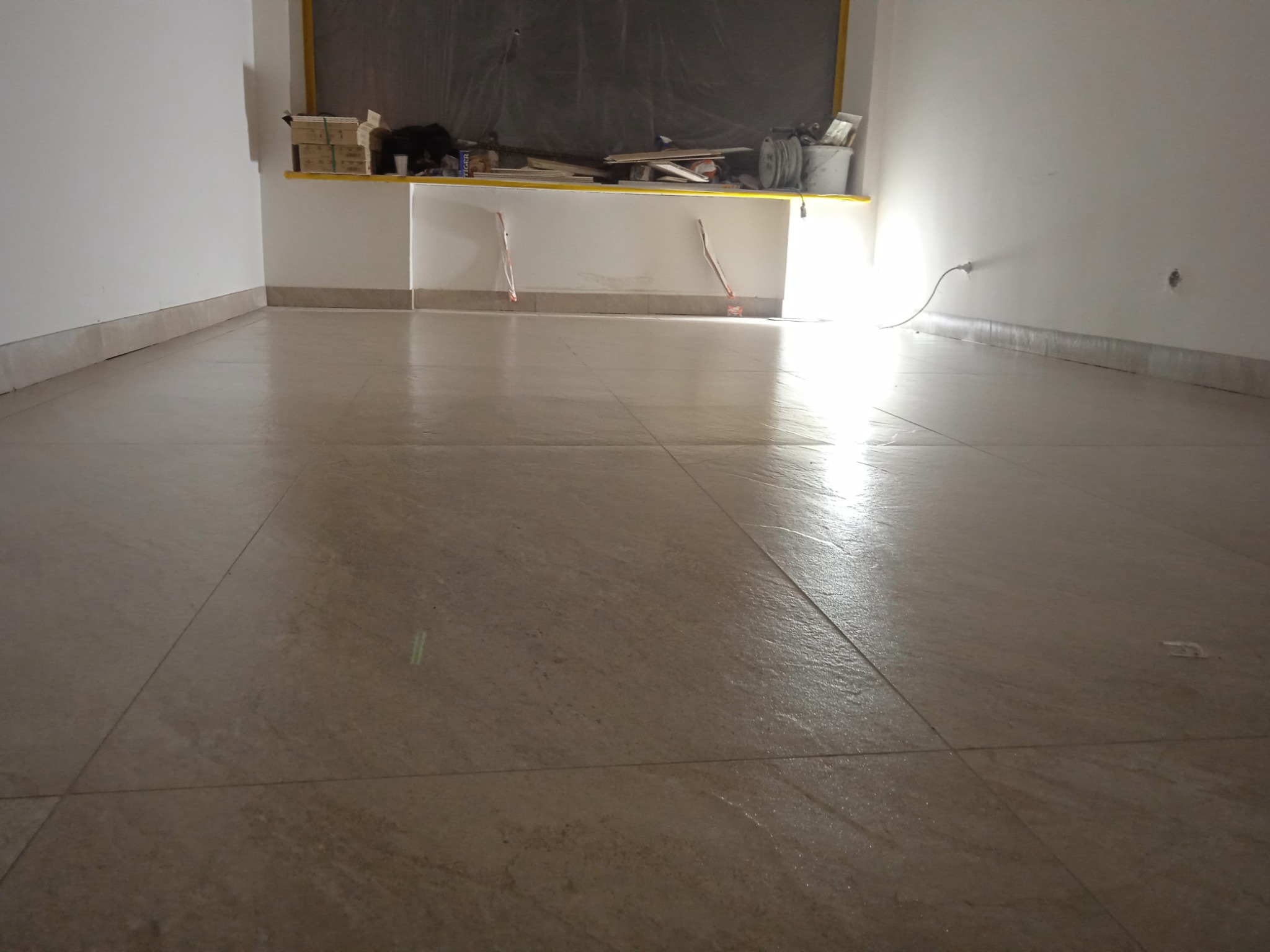 Beżowe płytki podłogowe ułożone w nowym pomieszczeniu. Widoczne narzędzia i materiały budowlane na półce w tle. Świeżo wykończona podłoga.